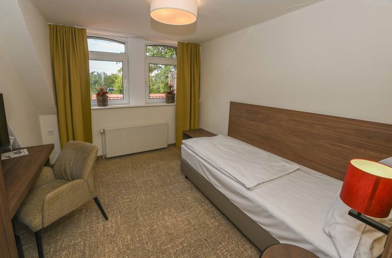 Modern eingerichtetes Einzelzimmer mit Bett und weiterer Sitzgelegenheit.