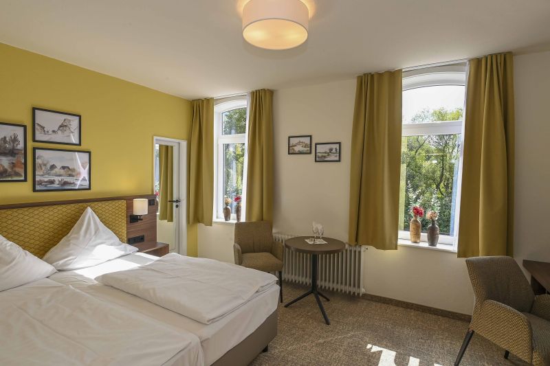 Modern eingerichtetes Doppelzimmer mit Doppelbett, Schreibtisch und weiterer Sitzgelegenheit.
