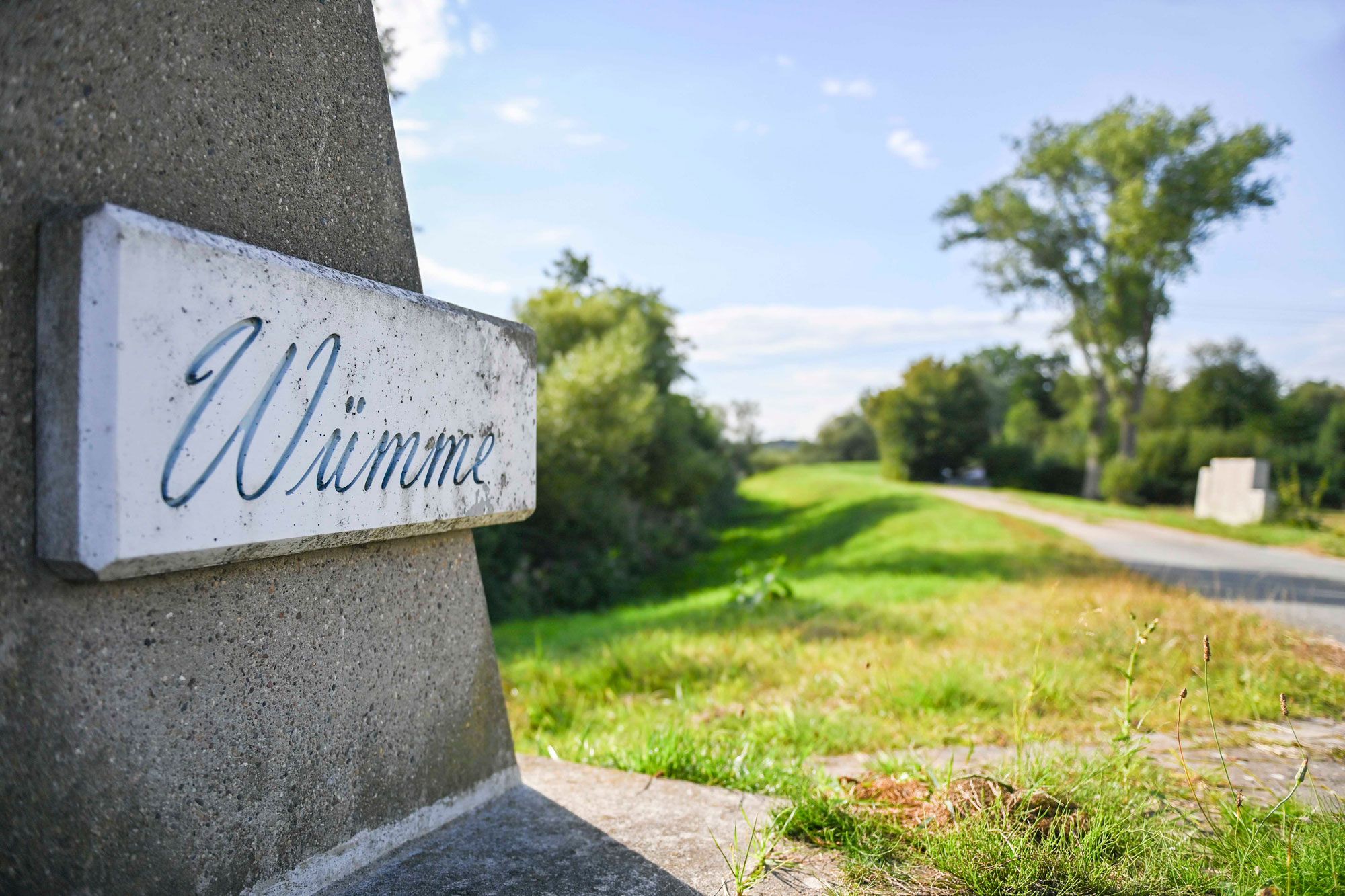 Beschriftung „Wümme“ auf einem Steinschild am Rand eines Fahrradweges