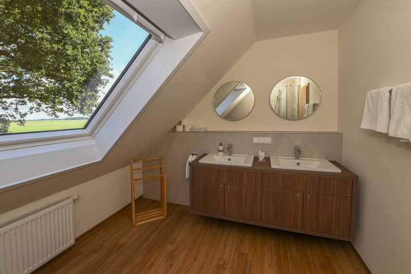 Geräumiges Badezimmer im Dachgeschoss, mit zwei Waschbecken und großem Fenster mit Blick in die Natur.