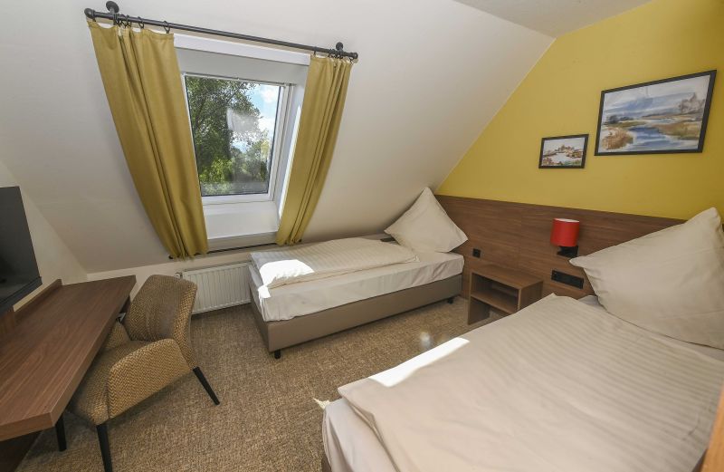 Modern eingerichtetes Doppelzimmer im Dachgeschoss mit zwei Einzelbetten und Sitzgelegenheit am Schreibtisch.