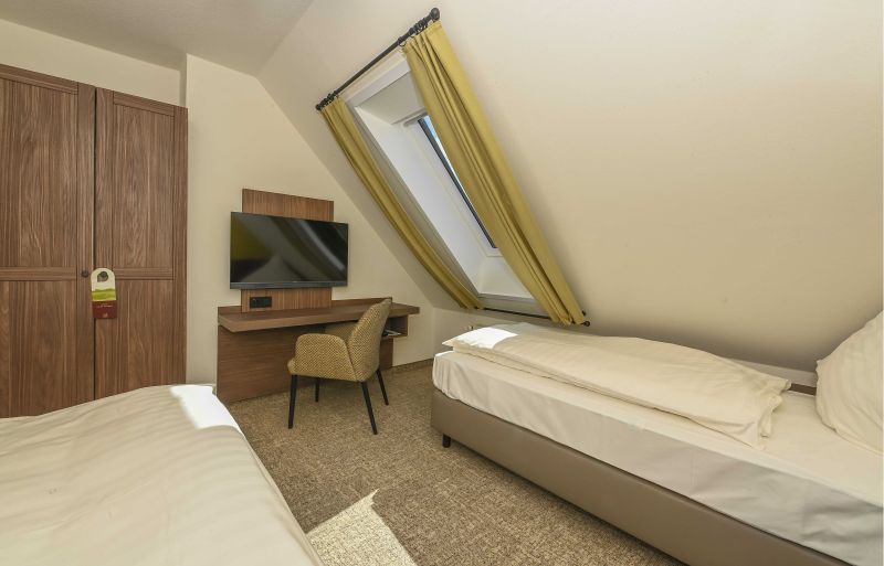 Modern eingerichtetes Doppelzimmer im Dachgeschoss mit zwei Einzelbetten, Kleiderschrank, Schreib- und Sitzgelegenheit und Flachbildfernseher.