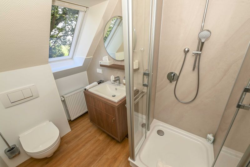 Modernes Badezimmer im Dachgeschoss mit Dusche, Waschgelegenheit, WC und Fenster mit Blick in die Natur.