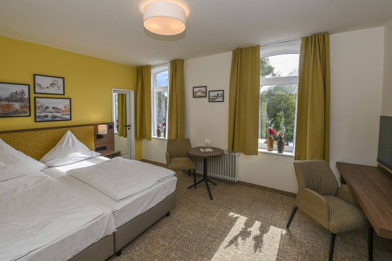Modern eingerichtetes Doppelzimmer mit Doppelbett, Schreibtisch und weiterer Sitzgelegenheit.